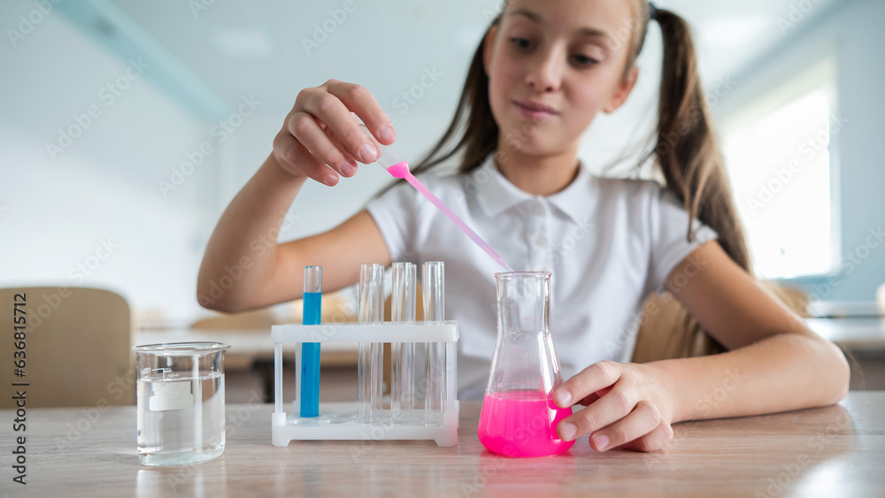 A schoolgirl conducts experiments in a chemistry lesson. Girl pouring colored liquids from a beaker. A schoolgirl conducts experiments in a chemistry lesson. Girl pouring colored liquids from a beaker.
