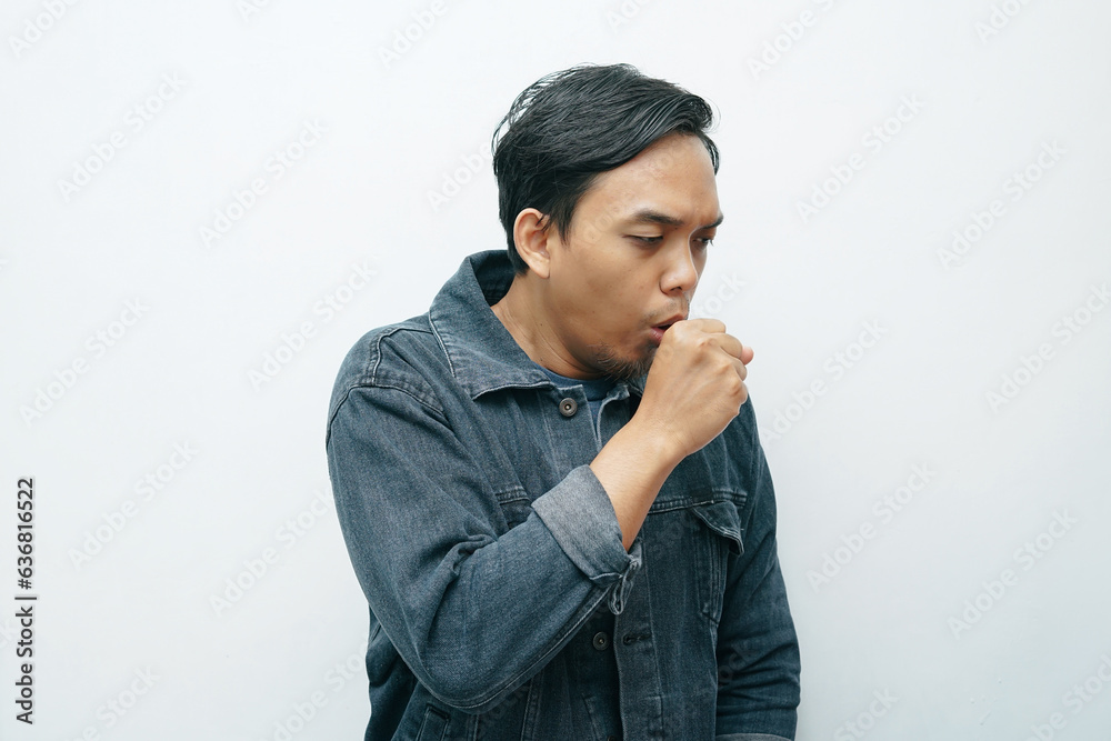 Portrait of Indonesian Asian man coughing and covering his mouth with hand clenched into a fist. Isolated white background Portrait of Indonesian Asian man coughing and covering his mouth with hand clenched into a fist. Isolated white background