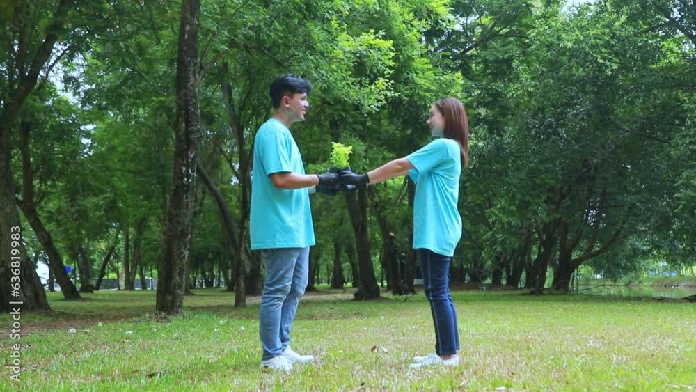 Couples young Asian male and female volunteers walk with saplings to plant trees to protect the environment in the garden to increase greenery. Let's grow together in the garden, smiling proudly. Couples young Asian male and female volunteers walk with saplings to plant trees to protect the environment in the garden to increase greenery. Let's grow together in the garden, smiling proudly.
