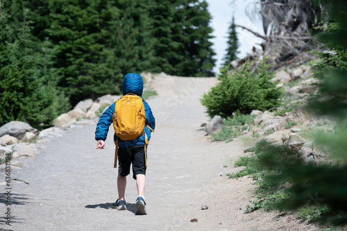 young child wearing a backpack and jacket on a hike up a dusty trail. 
