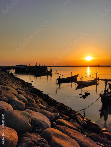 sunset on paiton beach with silhouettes of fishing boats anchored in the harbour photo