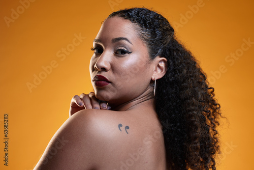 Beauty, portrait and a woman with a tattoo in studio for cosmetics, makeup and dermatology. Closeup of a young female model on an orange background in studio with body art, confidence and skin glow