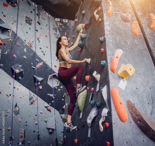 A strong female climber climbs an artificial wall with colorful grips and ropes.