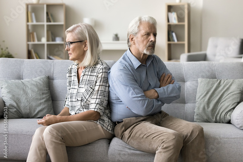 Annoyed ignoring senior couple sitting on home couch back to back, looking away, keeping silence after arguing, thinking on breakup, separation, relationship problems, conflict photo