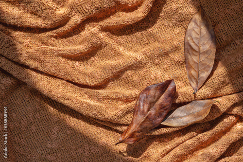 Brown dry fall leaves on terracotta, rust color knitted cloth crumpled messy background with natural sunlight shadows. Aestheric autumn backdrop, business brand template photo