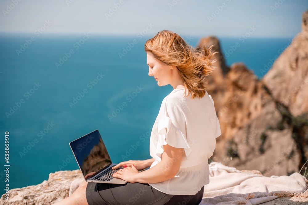 Freelance woman working on a laptop by the sea, typing away on the keyboard while enjoying the beautiful view, highlighting the idea of remote work.