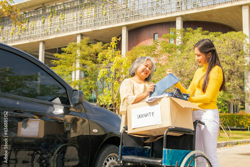 Foto Elderly mother and her asian philanthropist daughter drive to the shelter to donate wheelchairs and necessary charity clothes in cardboard boxes to the disabled and victims in need