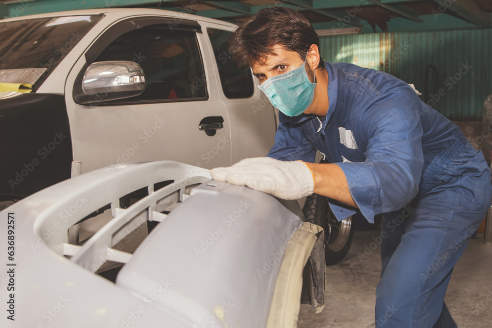 Meticulous male worker painters wearing dust masks for health care, cleaning up the surface of pickup truck bumpers, spraying primer, checking to bring to the painting room in the garage. Meticulous male worker painters wearing dust masks for health care, cleaning up the surface of pickup truck bumpers, spraying primer, checking to bring to the painting room in the garage.