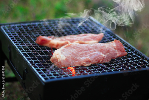 Smoke from the pork grilled on the grill of a black camping stove.