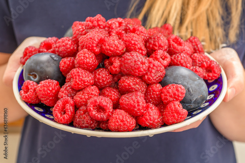 Trzymać w dłoniach talerz pełny soczystych świeżych owoców malin i śliwek 