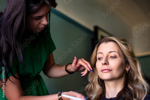 Makeup artist woman make up for lovely middle age lady at home, makes wizard image, close-up. Customer service in living room to create an amazing image. Make up creation concept. Copy ad text space