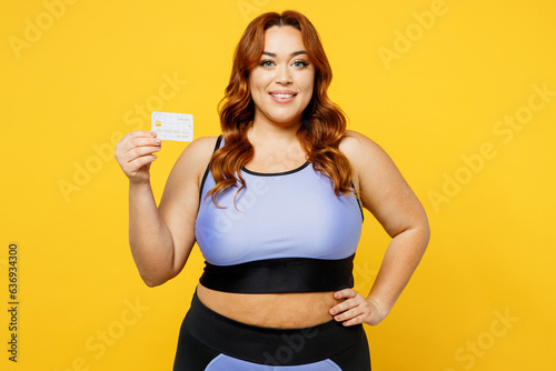 Young chubby overweight plus size big fat fit woman wear blue top warm up training hold in hand mock up of credit bank card isolated on plain yellow background studio home gym. Workout sport concept. © ViDi Studio