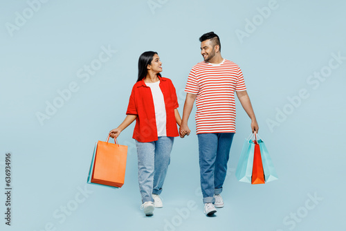Full body young couple two friend family Indian man woman wear red casual clothes hold package bags after shopping go isolated on plain blue color background studio. Black Friday sale buy day concept.
