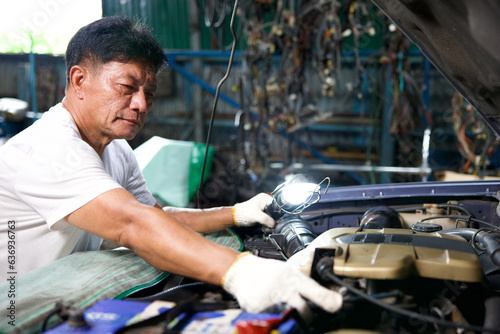 mechanic using flashlight for checking and fixing a car in automobile repair shop