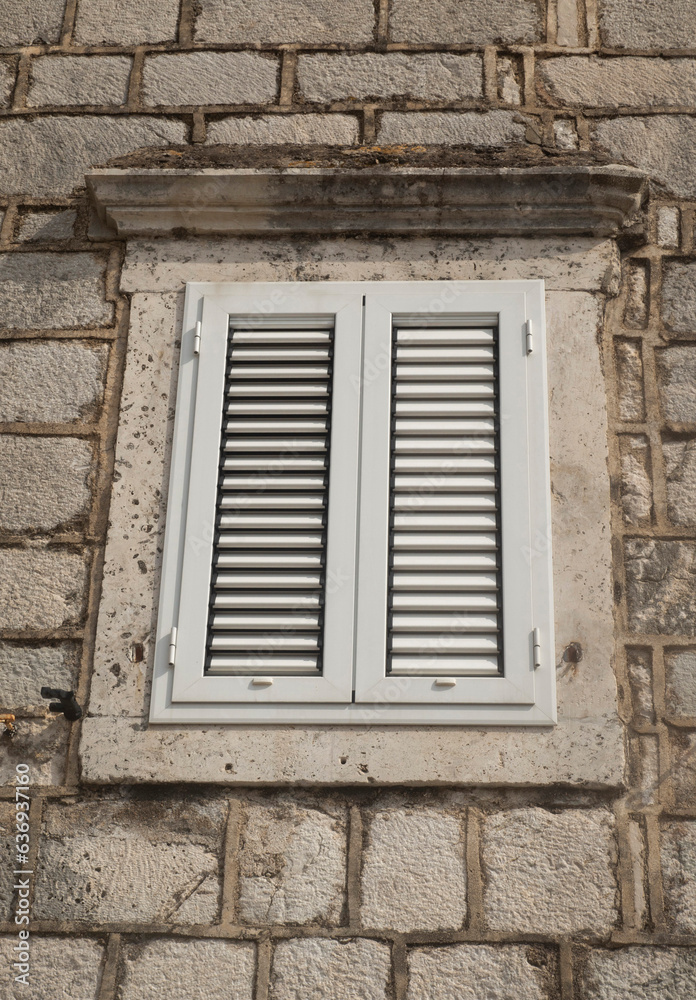 Traditional new white window shutters as blinds on old stone home