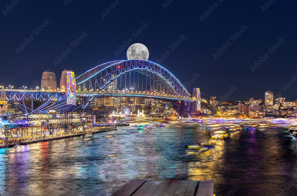 Obraz premium Panoramic night view of Sydney Harbour and City Skyline with a Sturgeon full Moon NSW Australia bright neon lights reflecting off the water