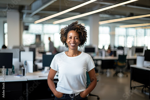 Adult smiling afro female office worker standing in a blank white t-shirt on a blurred office background. Mock-up for design. Blank template.