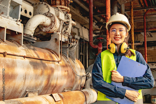 Photography Asian female technician worker in engineering department wearing hard hat supervising machinery refrigeration system factory holding tablet checking control system standing and looking at work place