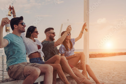 Group of joyful young people enjoying cold beer while spending fun time on the beach together © gstockstudio