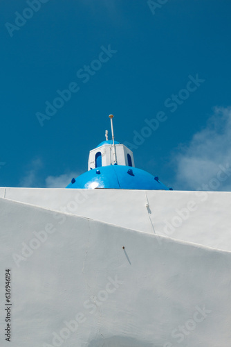 Close up of the dome of a Greek Orthodox Church in Santorini. Half sky with dome, blue colour and half whitewashed wall. 