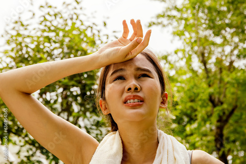 Asian woman doing sport jogging feeling sun and heat too hot during jogging in park sweltering summer weather covering face with hands covering face against UV rays : Sun protection health care concep