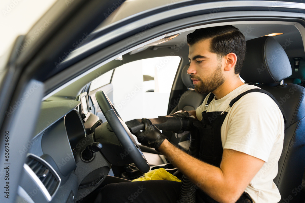 Professional cleaner vacuuming steering wheel of a car at service station