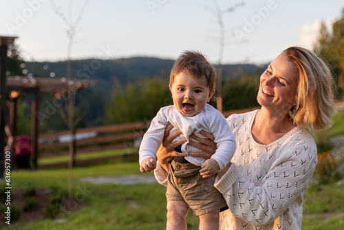 Smiling baby boy on mother hands enjoy play in home garden