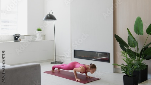 Athletic young female exercising, stretching and doing yoga in morning in bright sunny room at home. Attractive woman in sports clothes doing gymnastic bridge on mat