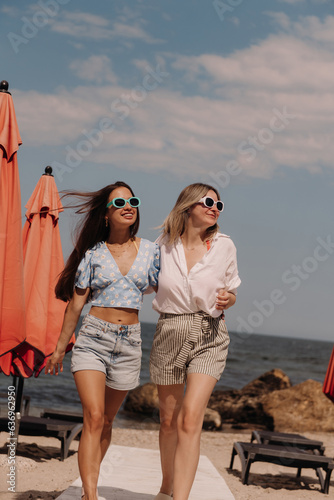 Two joyful young women embracing and smiling while walking by the beach together