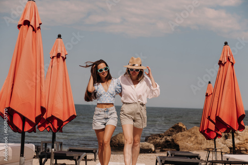 Two beautiful young women embracing and smiling while walking by the beach together