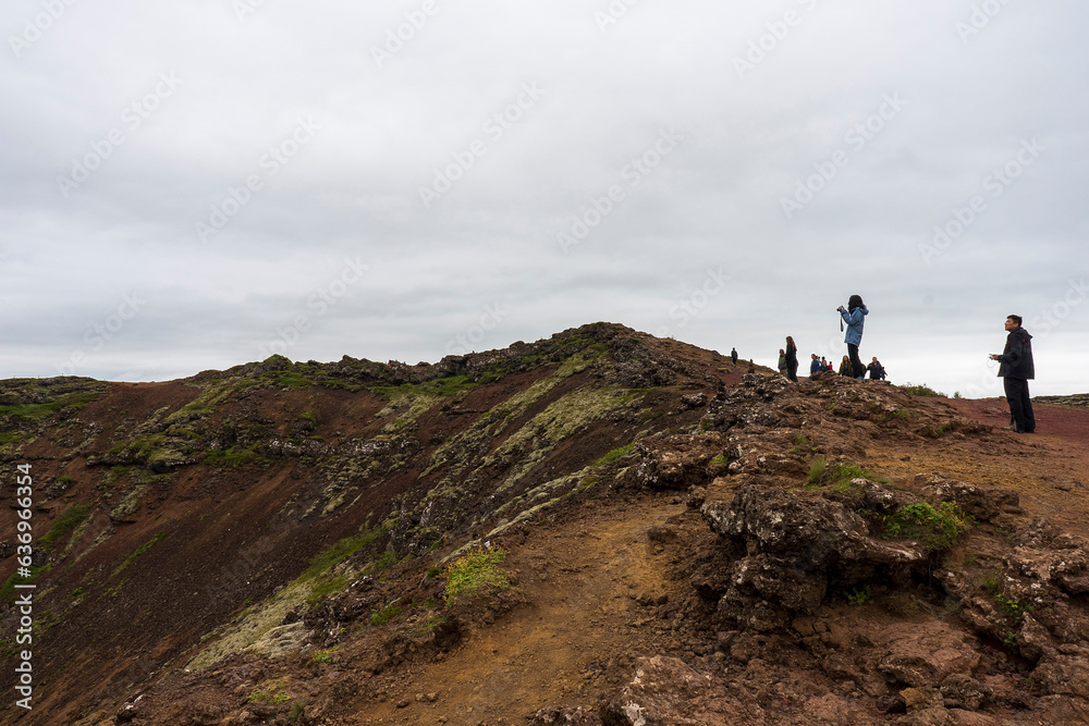 People walking on upper ridge of the volcanic Kerid Crater overlooking the crater lake in the Grimsnes area of South Iceland. 