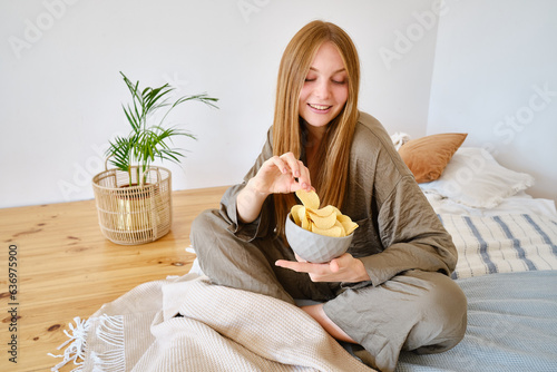 Foto A girl eats crispy potato chips from a bowl on the couch