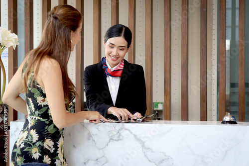 Canvastavla Beautiful smiling Asian receptionist suggests travel program for tourist woman customer, female staff at reception counter desk provides information, guest booking tour at a hotel on holiday vacation
