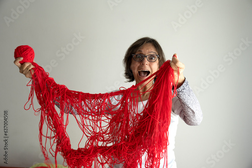 Senior woman is entangled with red wool and has a ball of yarn in her hand photo