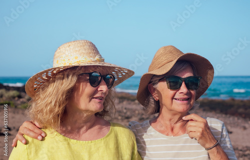Family couple of senior and middle aged women embraced standing outdoors at sea wearing sunglasses and hats. Vacation, freedom, friendship concept. Horizon over water © luciano