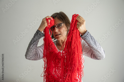 Senior woman is entangled with red wool and has a ball of yarn in her hand photo