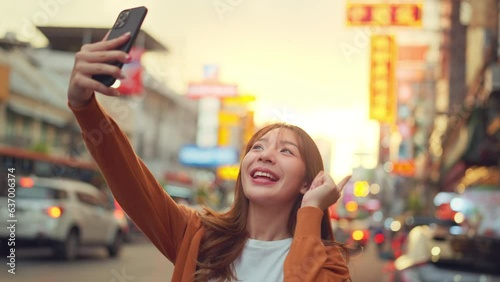 Happy young Asian tourist woman selfie by mobile smartphone, Female traveller taking photo of Chinatown street food market during sunset in Bangkok, Thailand, Summer journey trip concept. photo