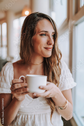 Chica joven tomando café en cafetería de hotel mientras mira por la ventana 