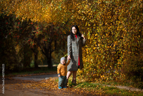 Mother and son having fun together in autumn park. Happy family walking in yellow trees in fall. Thanksgiving holiday. Happy motherhood and childhood concept. © sergiophoto