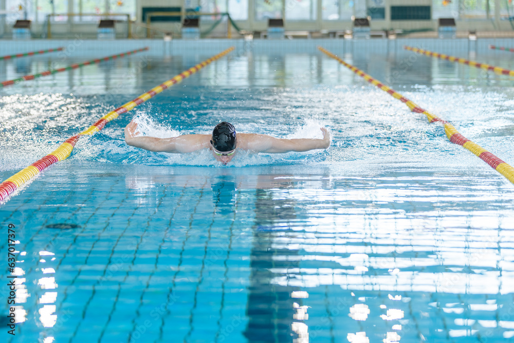 Professional male swimmer performing butterfly style in the indoor lap pool lane, front view. Success, motivation, and effort concept.