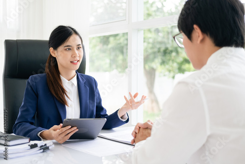 Portrait of investment advisor businesswoman sitting at desk in office with tablet and consulting with young professional man.