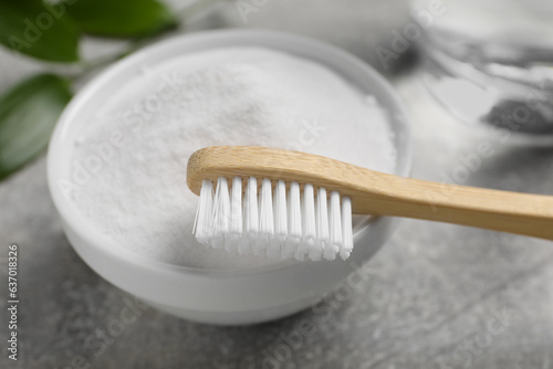 Bamboo toothbrush  green leaf and bowl of baking soda on grey table  closeup