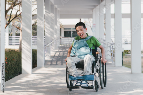 Asian child with a blue backpack smiling face with happiness wheelchair pushed by himself on the ramp of home or hospital,school,nursery,concept of facilities necessary for people with disabilities. photo