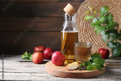 Delicious cider and apples with green leaves on wooden table, space for text