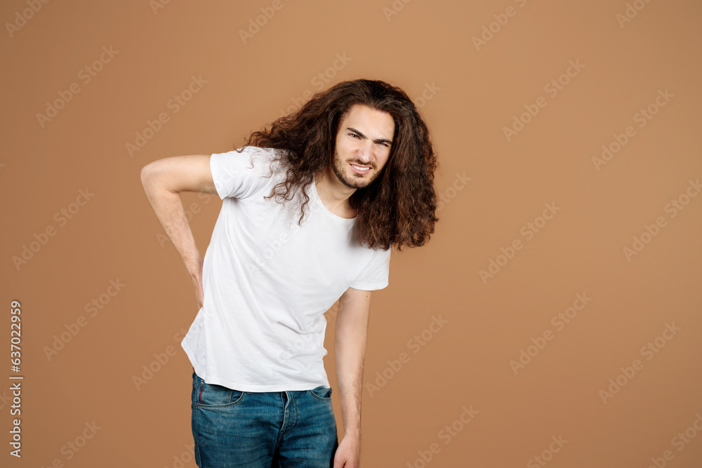 Hispanic guy touching back suffering from pain over beige background Hispanic guy touching back suffering from pain over beige background