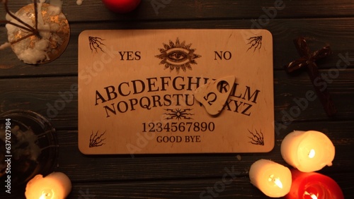 Картината върху платно Close up shot of a wooden ouija board with a planchette on a table surrounded by candles, candlesticks and other elements in a muffed warm light