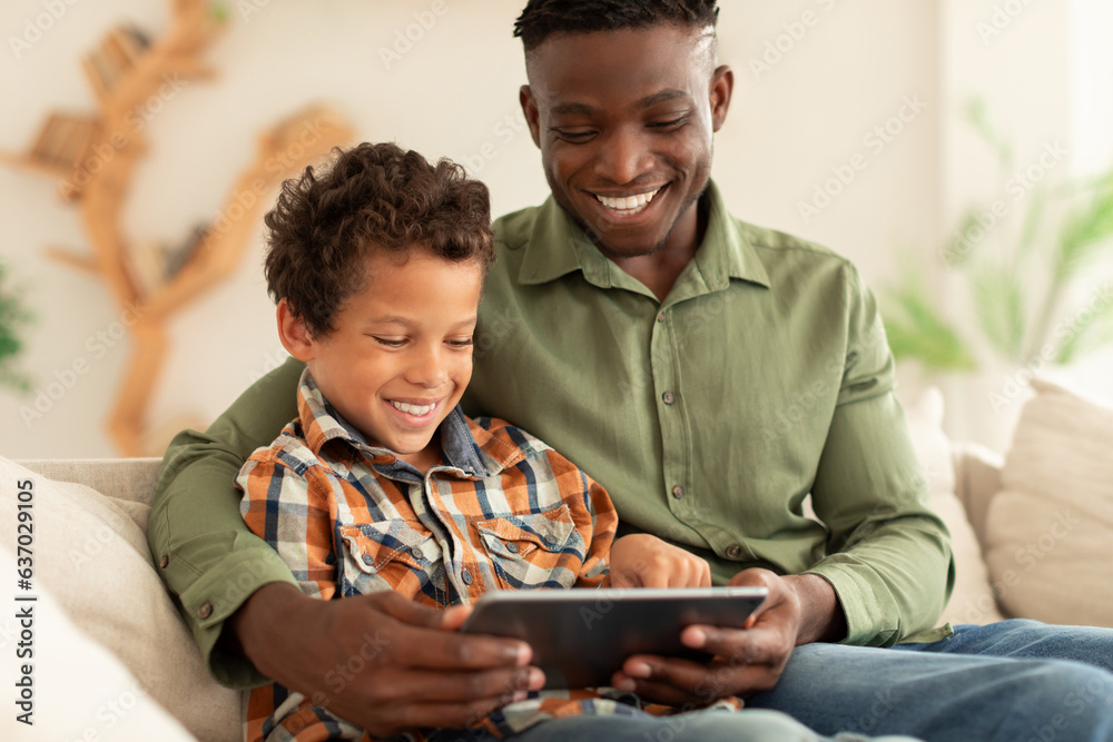 Happy Black Man And His Son Using Digital Tablet Indoors Happy Black Man And His Son Using Digital Tablet Indoors