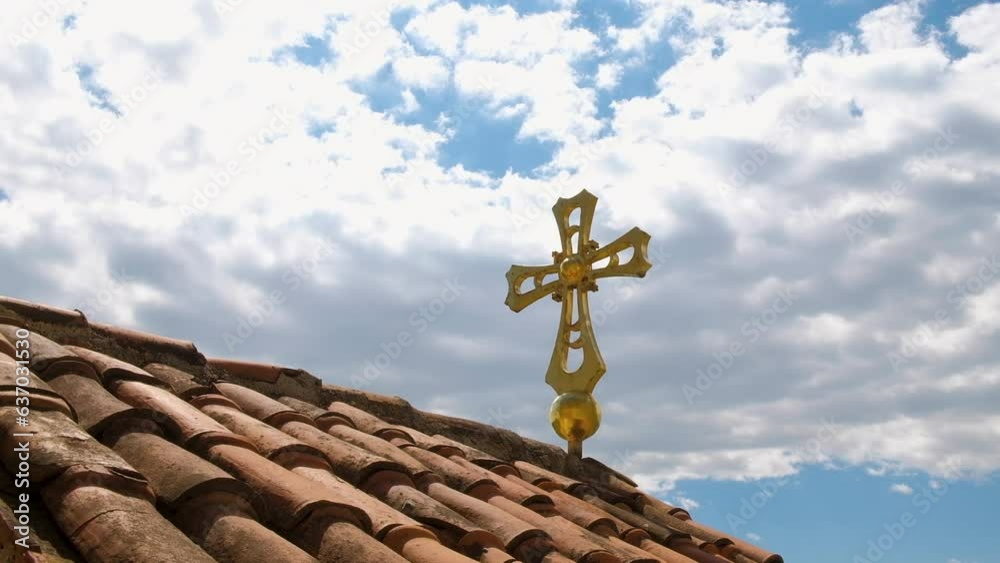 Golden Orthodox cross on old tiled roof, blue cloudy sky background Golden Orthodox cross on old tiled roof, blue cloudy sky background