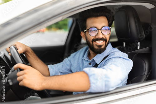 Cheerful indian man driving car, shot from outside, closeup © Prostock-studio