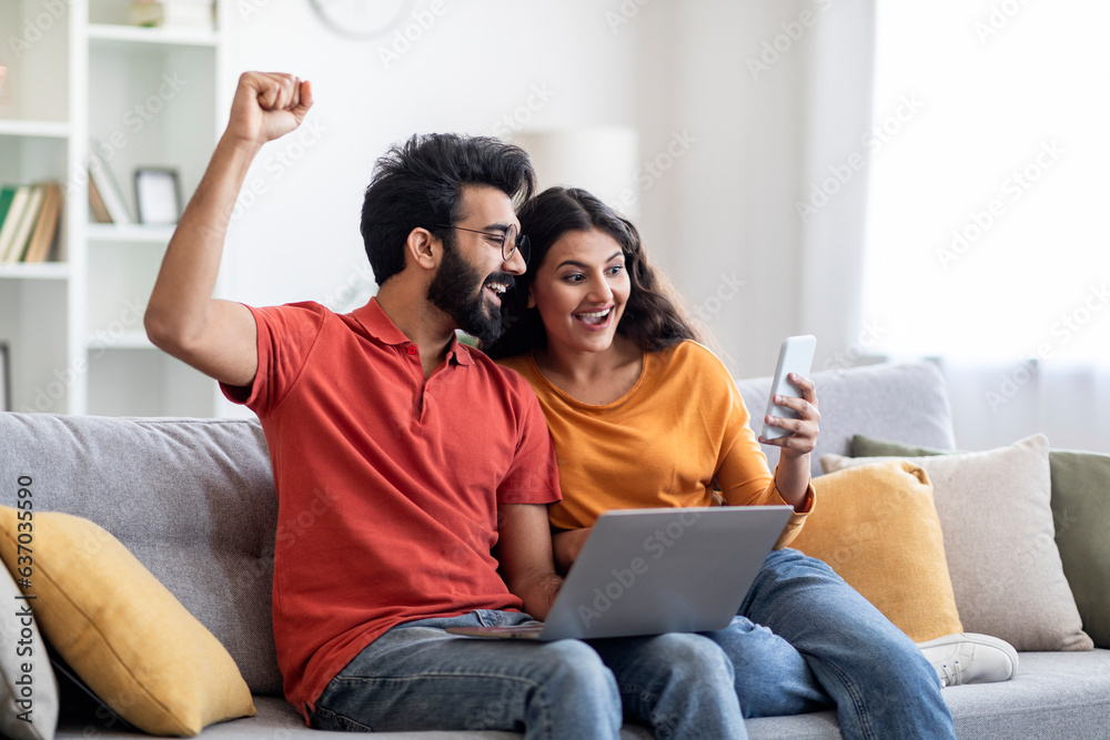 Online Win. Excited Indian Couple Celebrating Success With Smartphone At Home Online Win. Excited Indian Couple Celebrating Success With Smartphone At Home